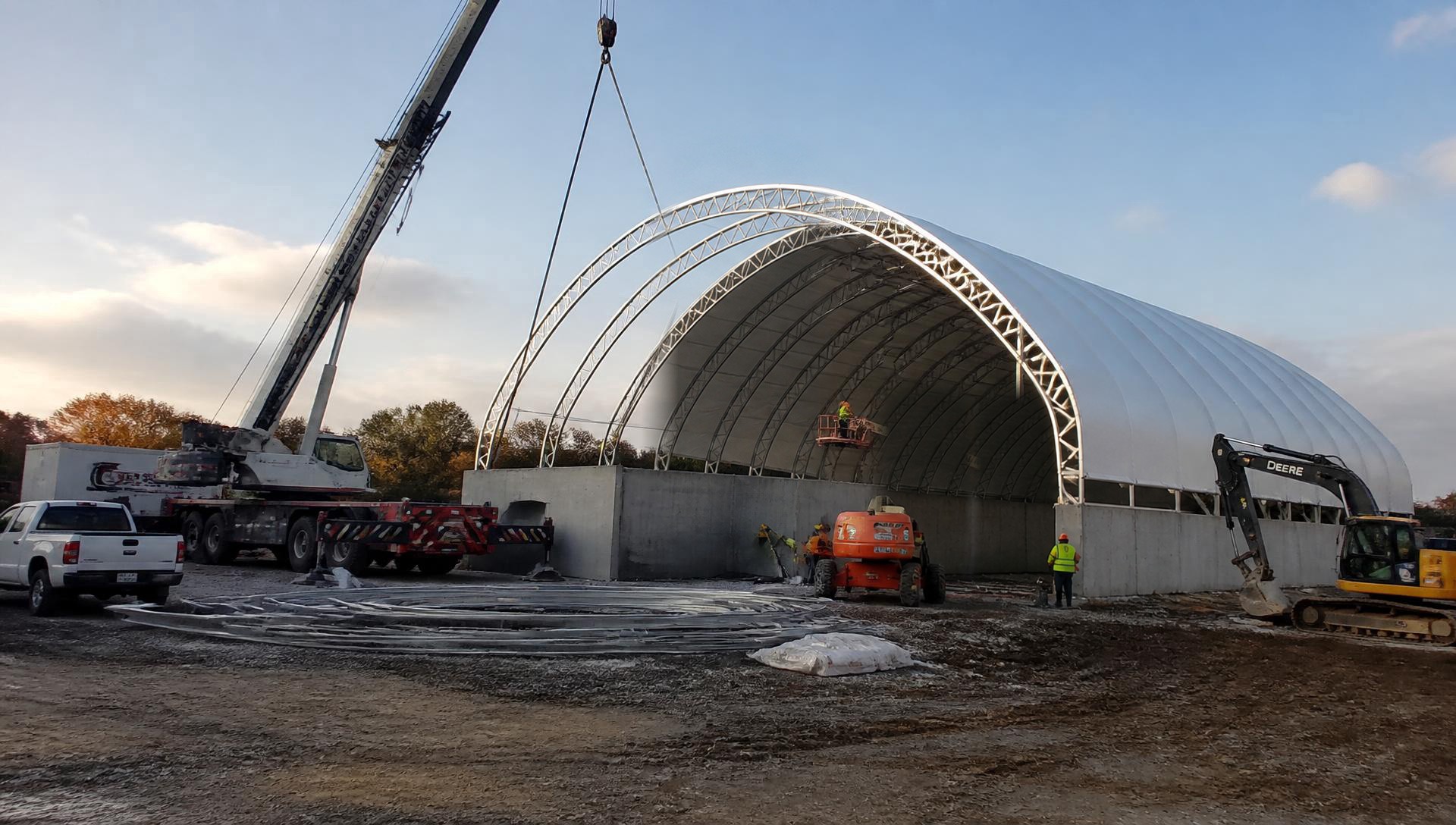 Crane and installation crew erecting galvanized steel arches of a MegaDome fabric building on concrete stem walls at an Ontario construction site