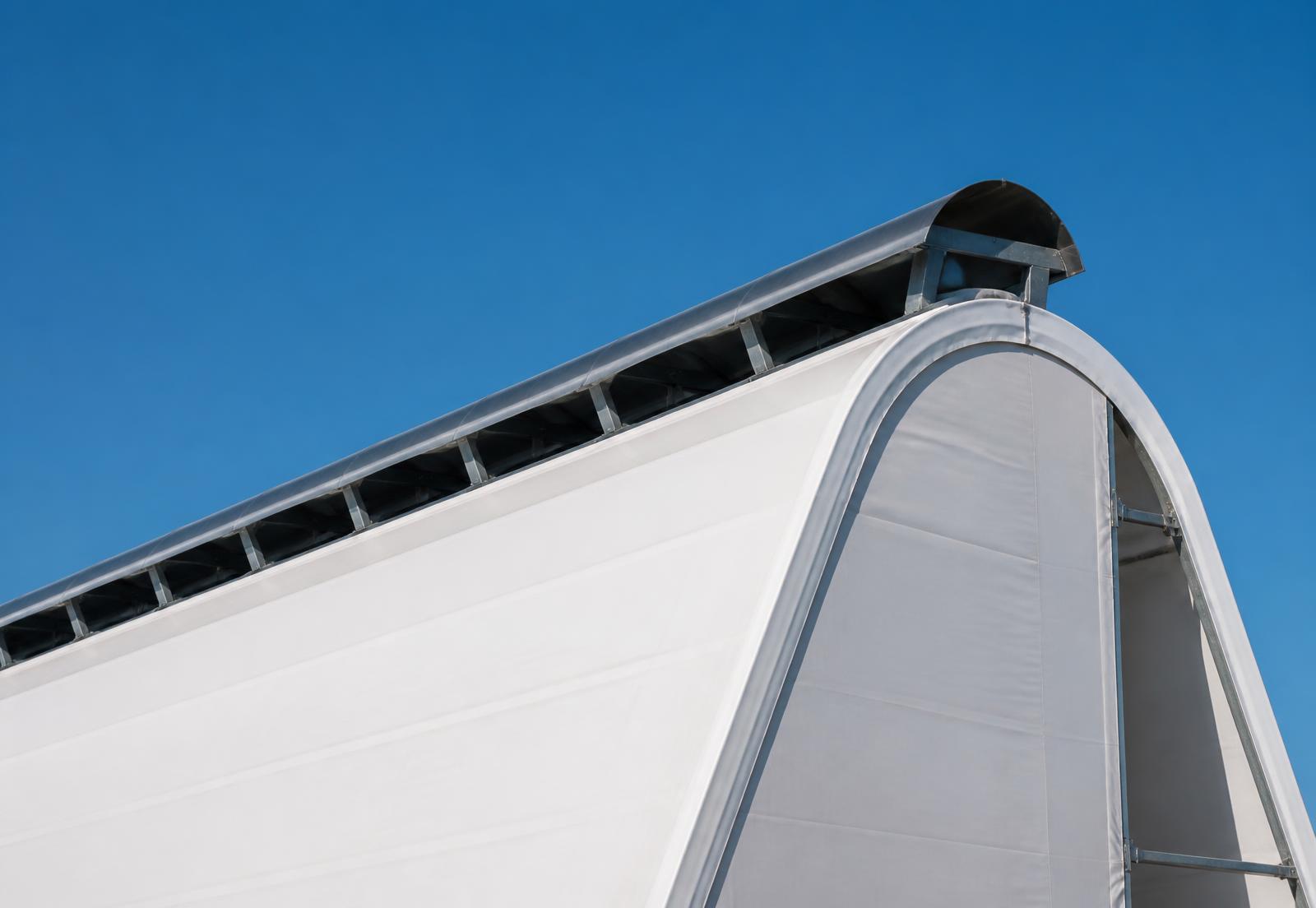 Continuous weather-hooded aluminum ridge vent running the full length of a white MegaDome fabric building peak