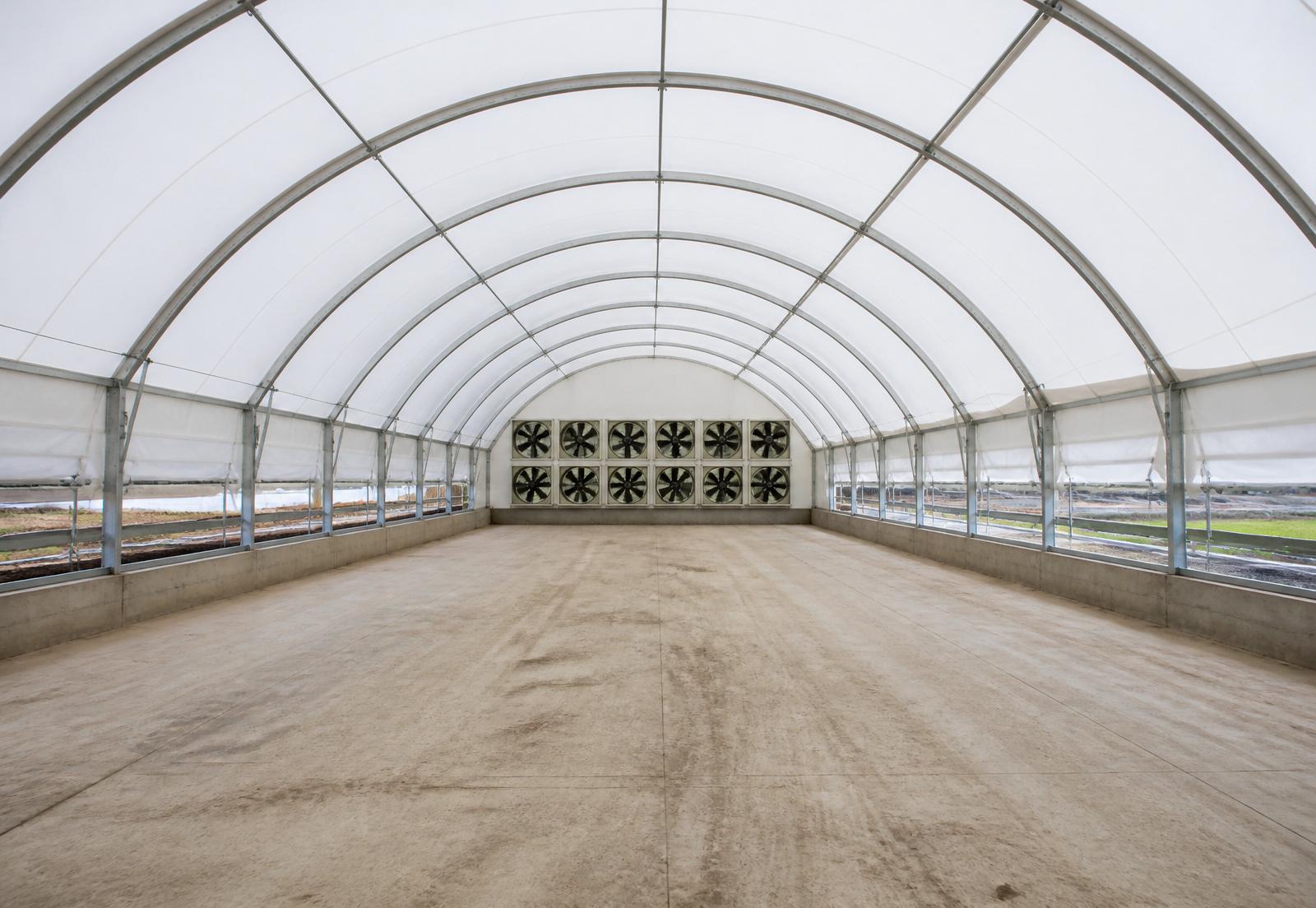 Interior of a long MegaDome fabric building with a full bank of tunnel-ventilation exhaust fans on the gable end and curtain sidewall inlets