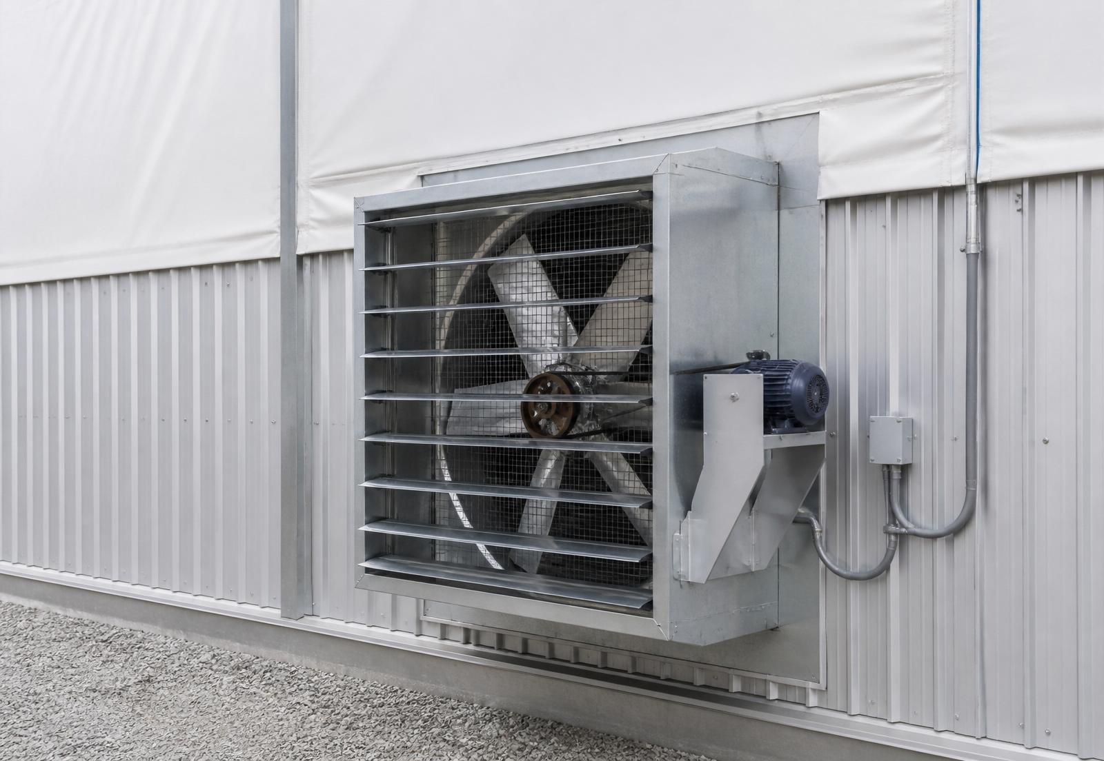 Heavy-duty belt-drive sidewall exhaust fan with galvanized housing and motorized shutters mounted on the steel wainscot of a fabric building